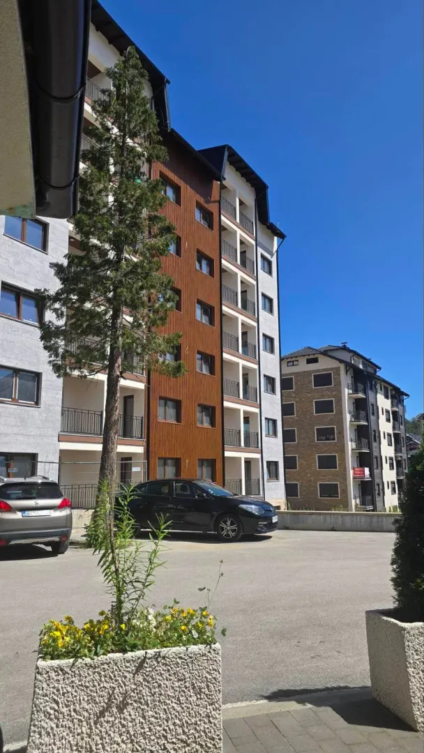 Spoljašnji izgled višestambene zgrade sa parkingom i zelenilom.