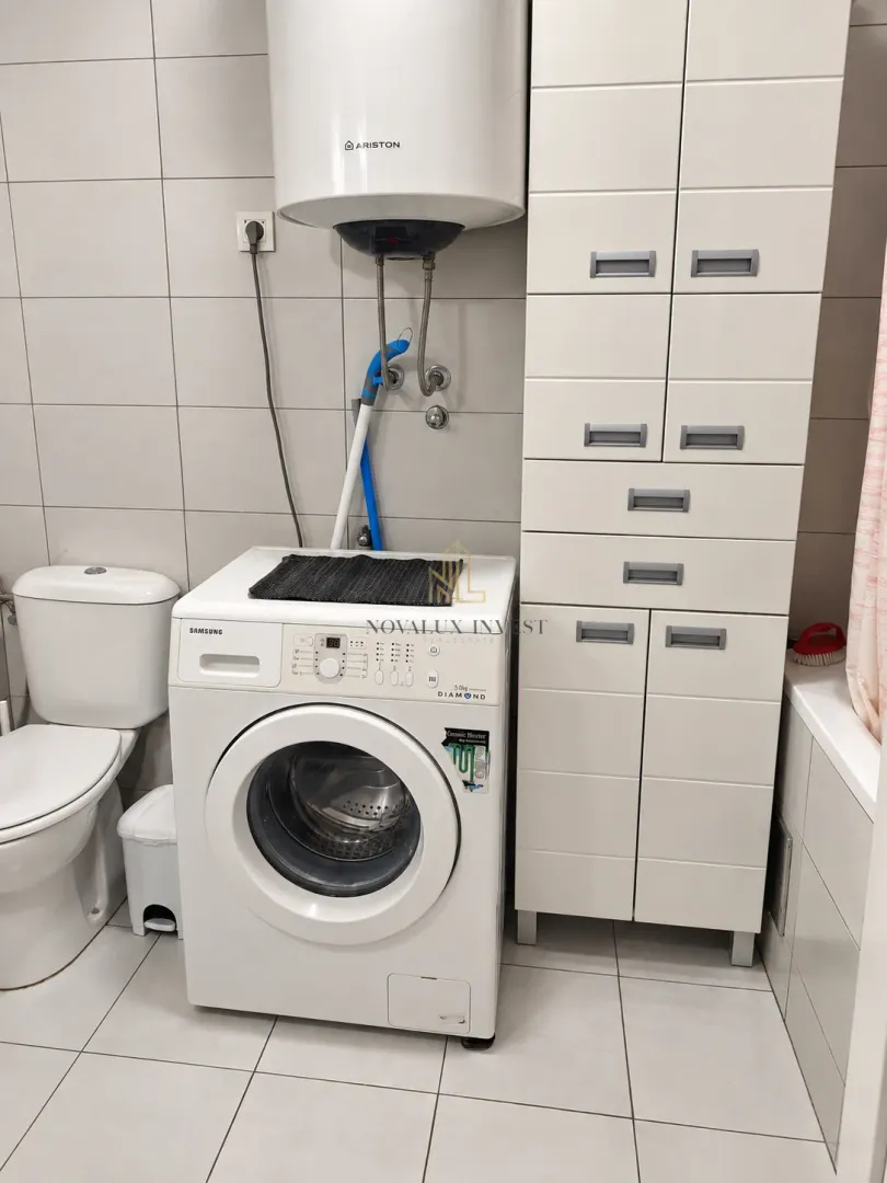 Kupatilo opremljeno sanitarijama, veš mašinom i bijelim ormarićem.