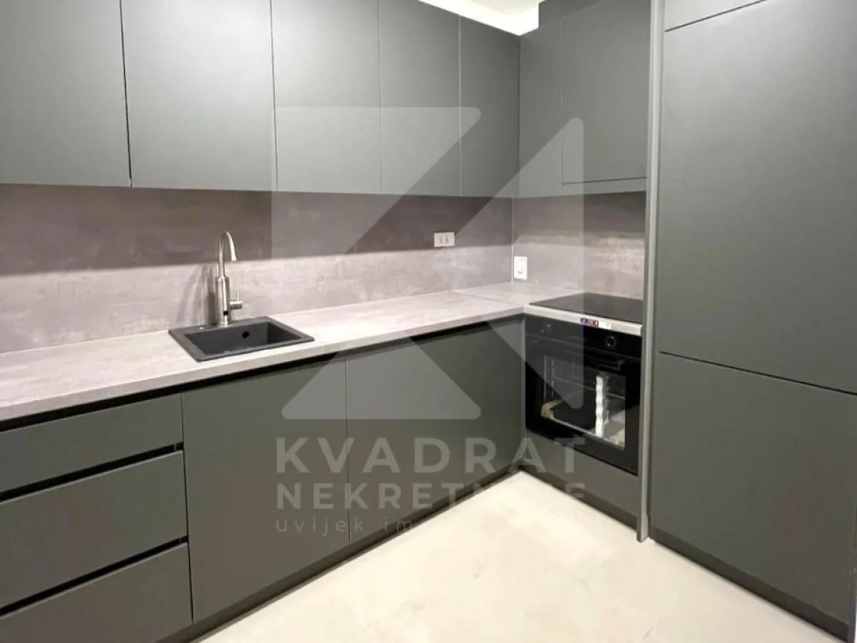Moderna kuhinja tamnih elemenata sa ugradnom rernom i sudoperom.