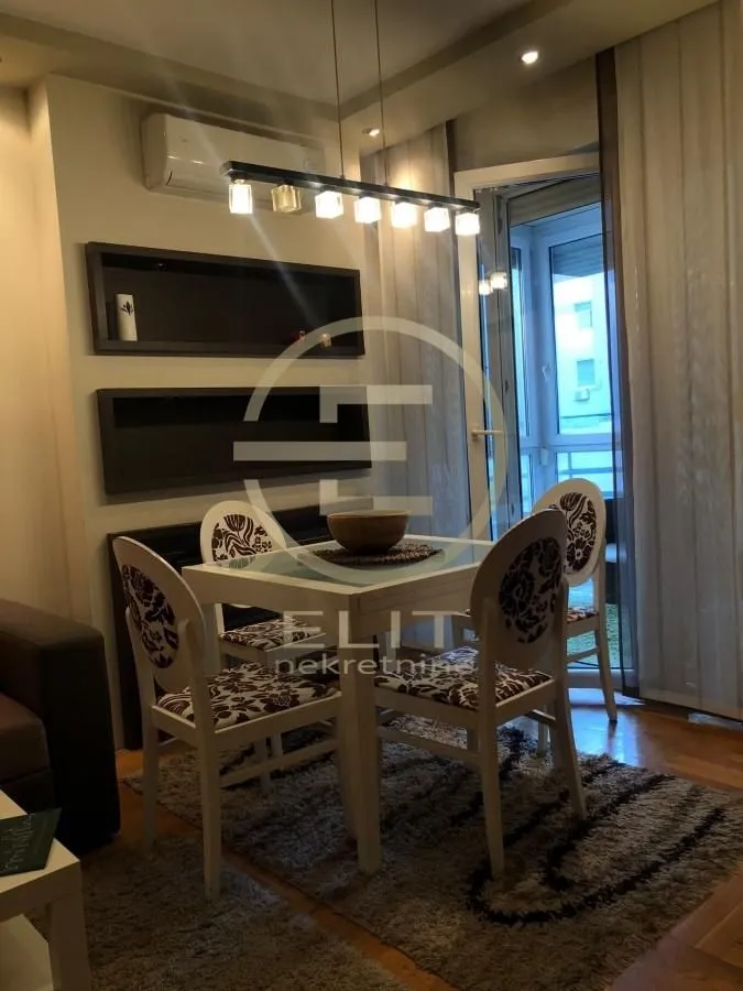 Trpezarija sa stolom i četiri stolice, smeštena u sklopu dnevnog boravka.