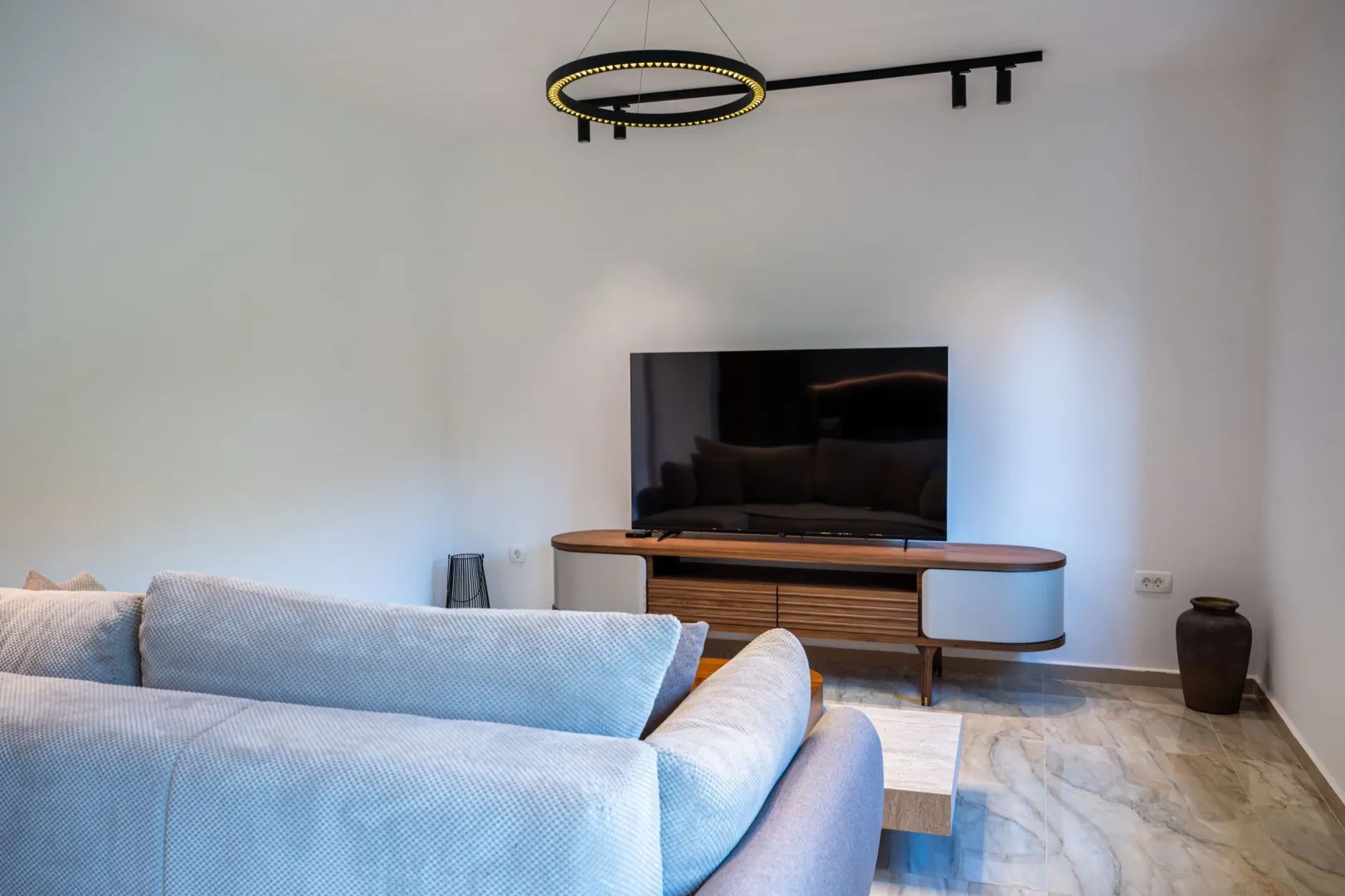 Dnevna soba sa ugaonom garniturom, televizorom i modernim osvjetljenjem.