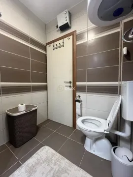 Compact bathroom with a toilet, laundry basket, and brown-toned tiles. - image 15