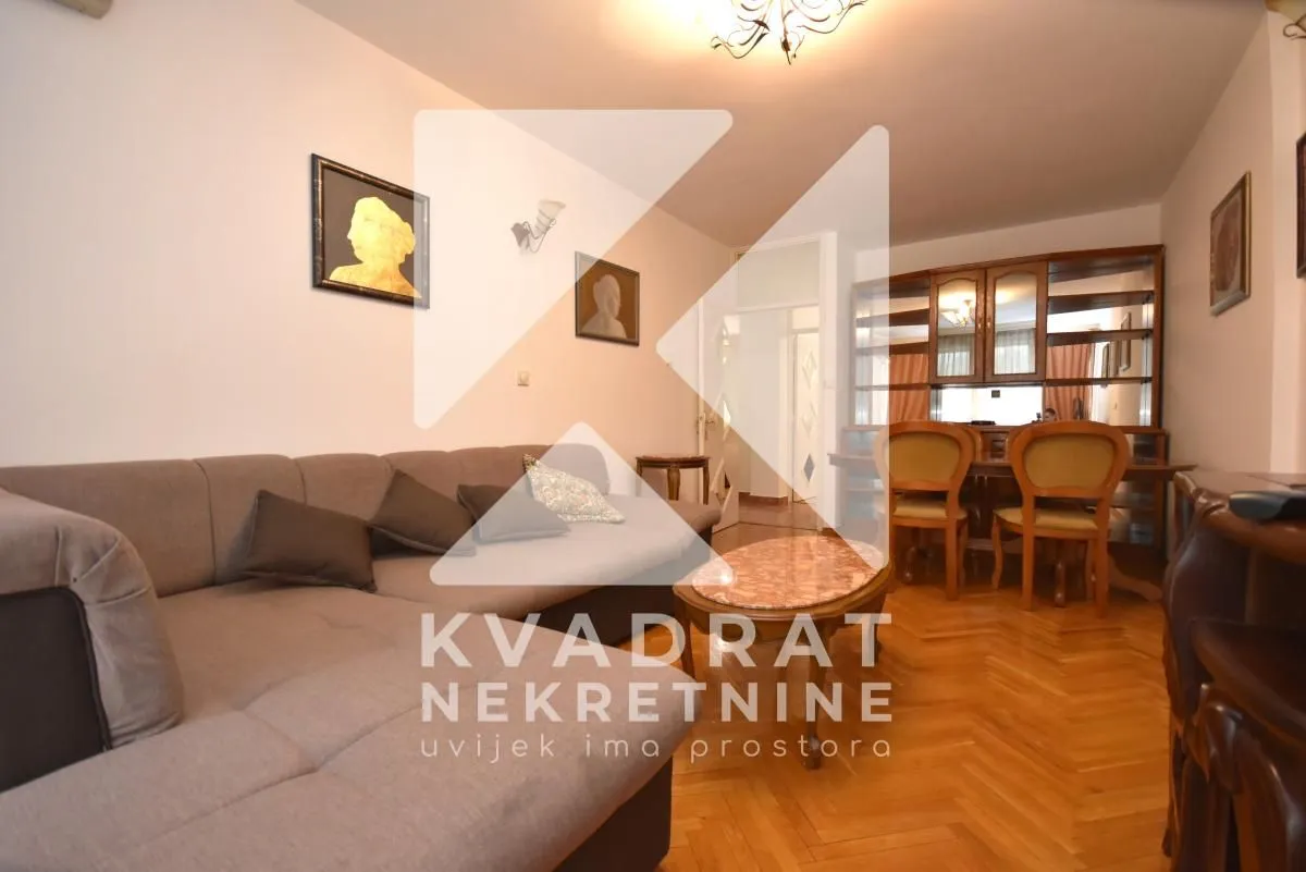 Living room with a sofa seating area and a dining space in the background.