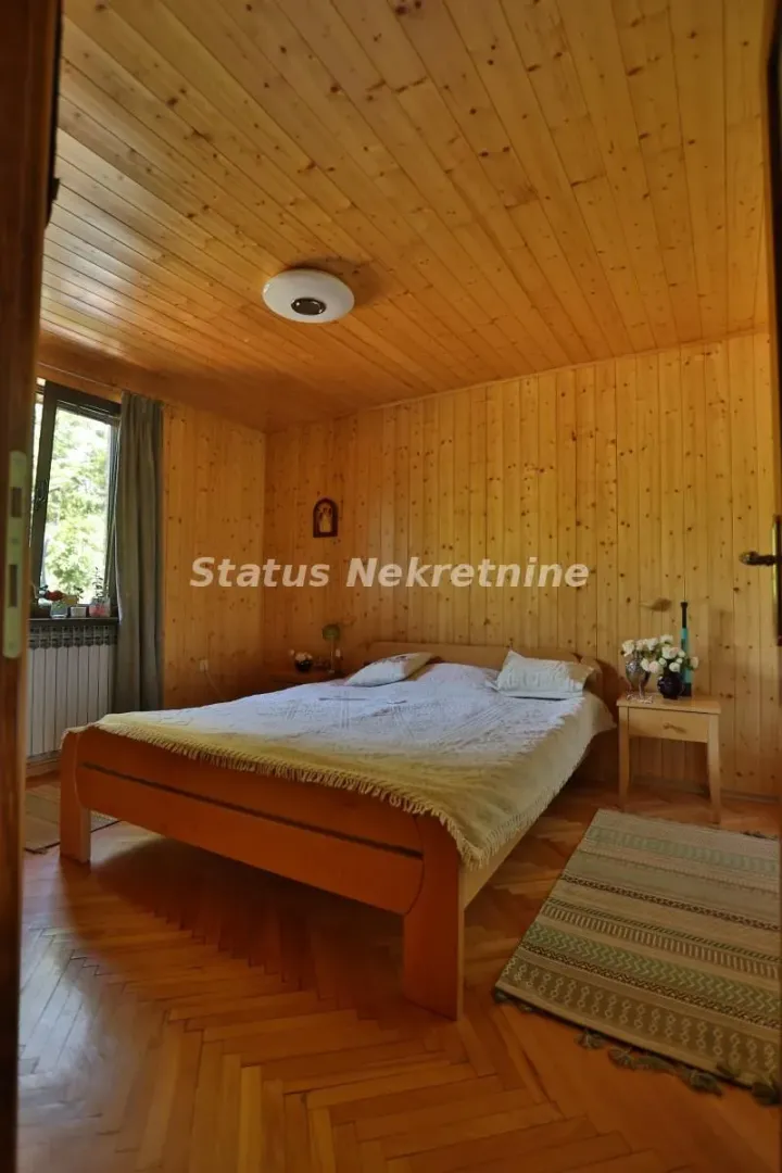 Spavaća soba sa drvenim oblogama na zidovima i plafonu i bračnim krevetom.
