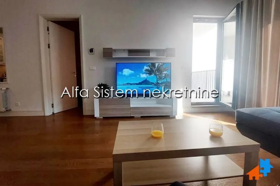 Dnevna soba sa televizorom, drvenim stočićem i izlazom na terasu.