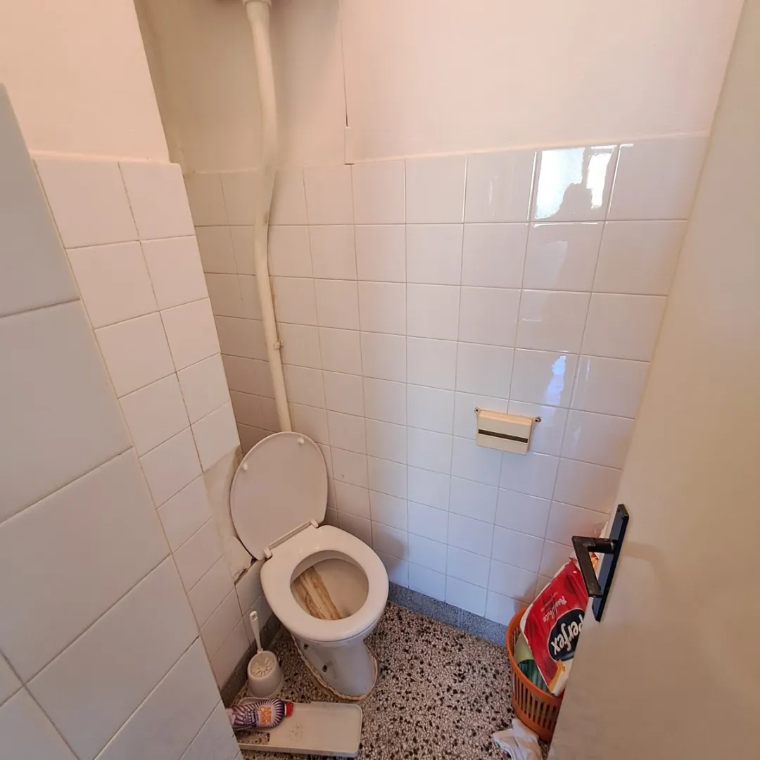 Manje kupatilo sa bijelim pločicama i WC šoljom.