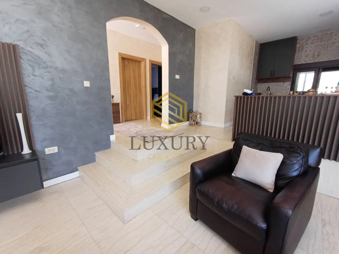 Living room with an armchair and a view of the kitchen and hallway.