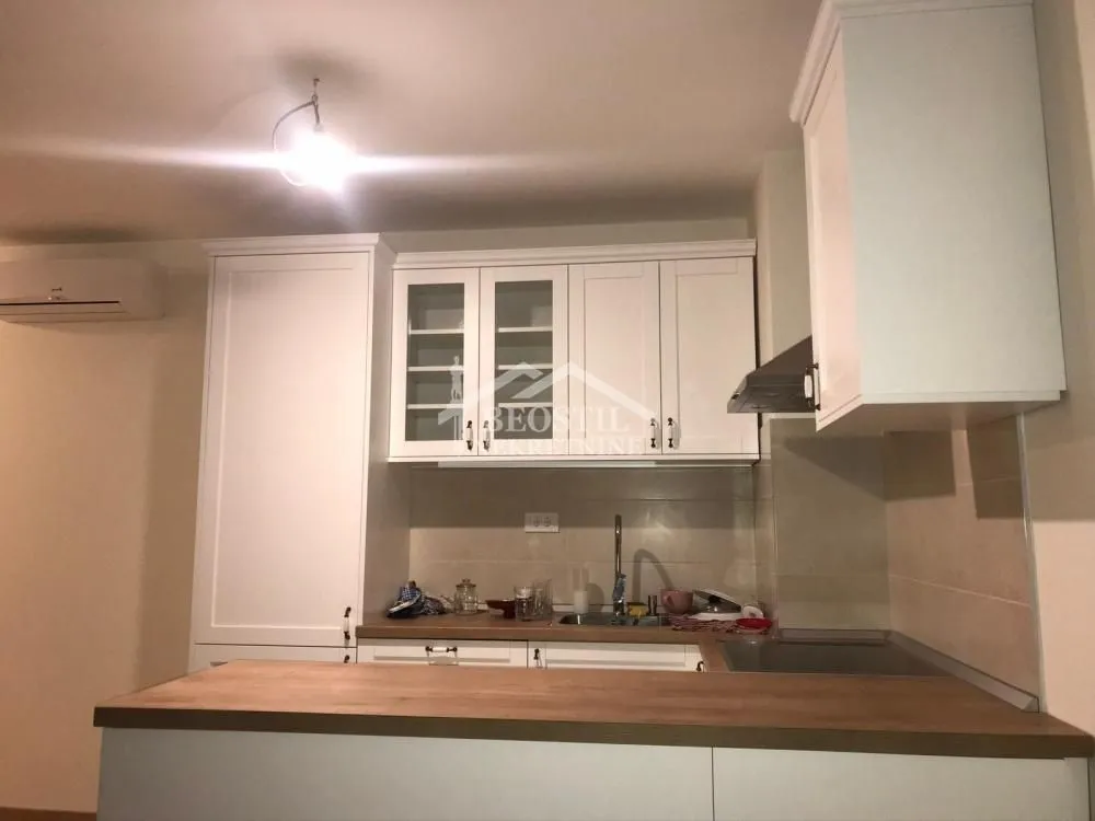 Manja bela kuhinja sa drvenom radnom površinom i gornjim elementima.