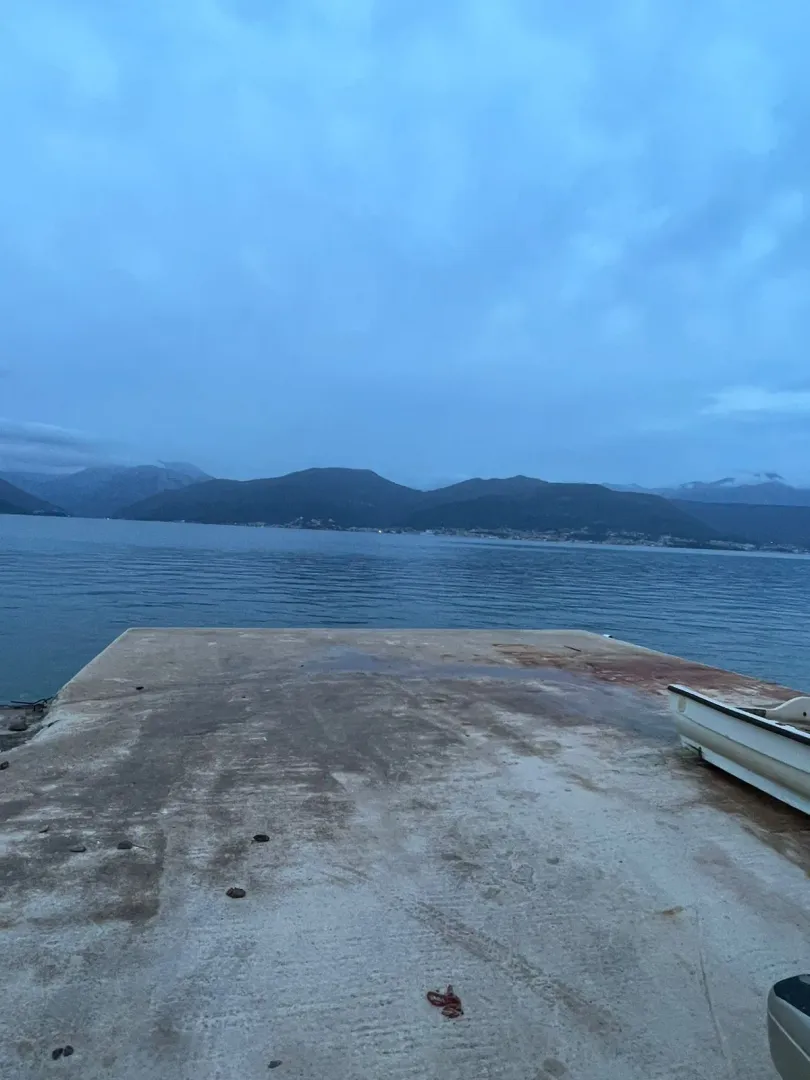 Betonska riva uz more sa pogledom na zaliv i planine.