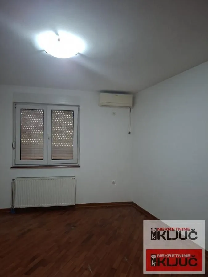 Prazna soba sa parketom, prozorom i klima uređajem.