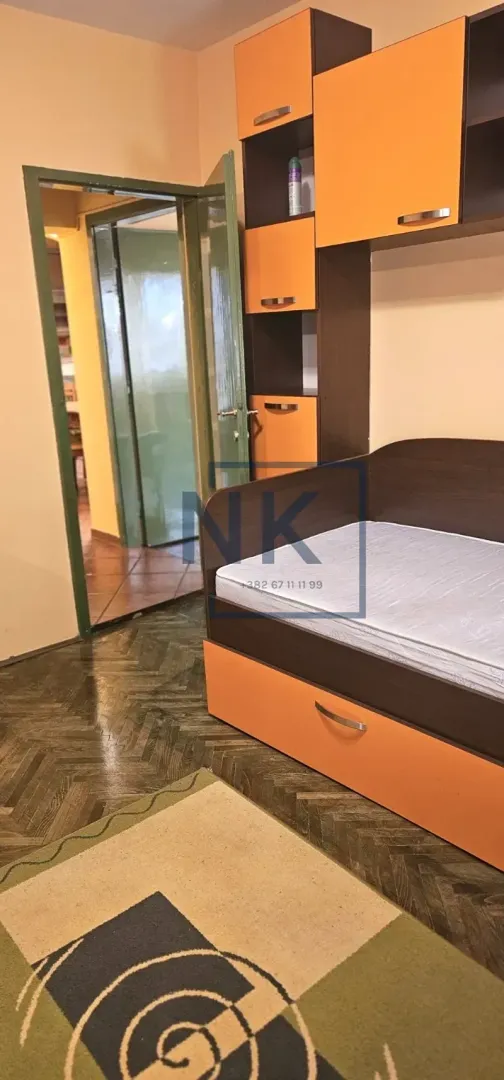 Manja spavaća soba sa krevetom i ugradnim ormarom u narandžastoj boji.