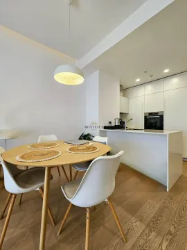 Dining area with a wooden table and chairs in a modern apartment with the kitchen in the background. - image 5