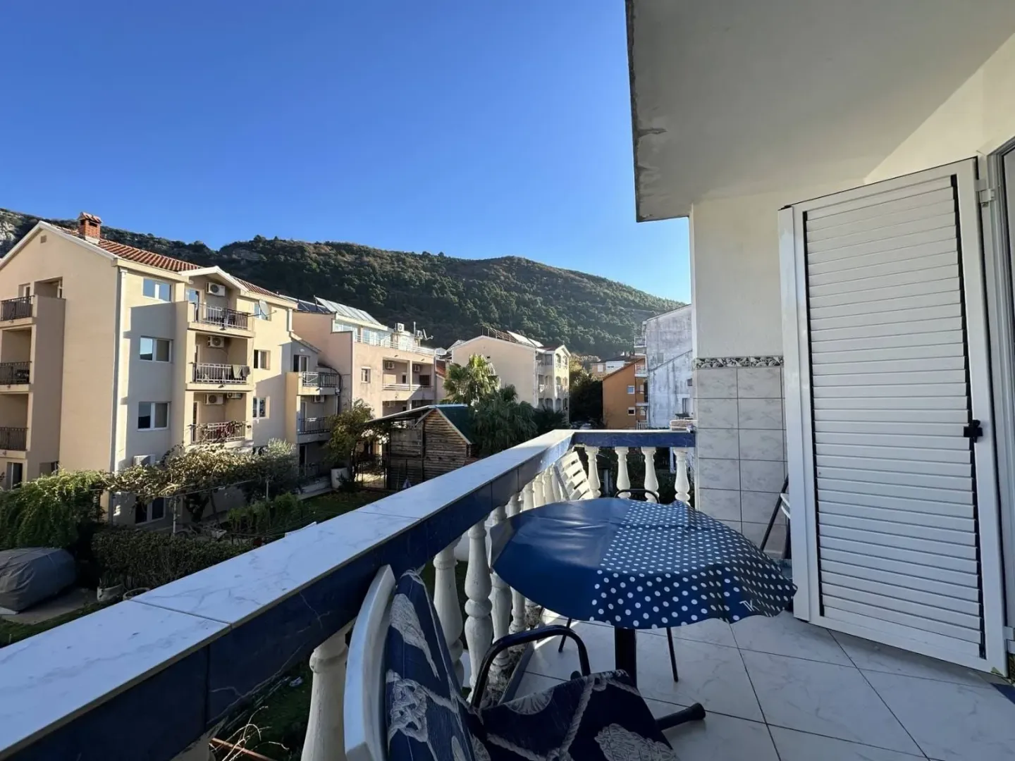 Covered balcony with seating set and view of surrounding buildings and hills.