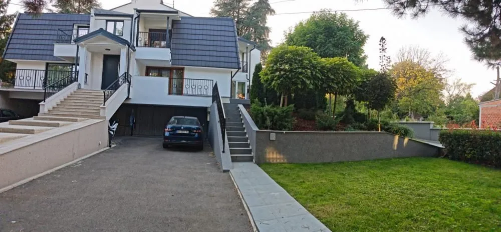 Pogled na prednju fasadu kuće sa dvorištem, parkingom i stepeništem.