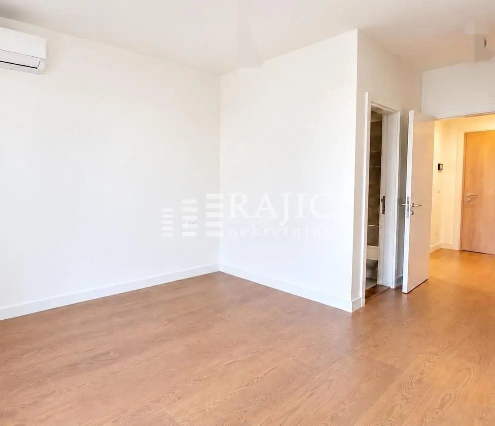 Empty room with light wooden flooring and white walls.