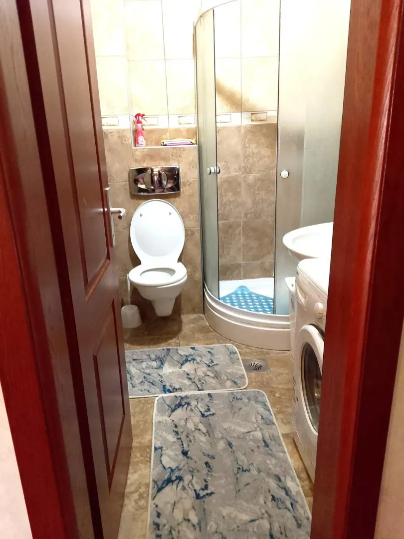 Manje kupatilo sa tuš kabinom, WC šoljom i veš mašinom.
