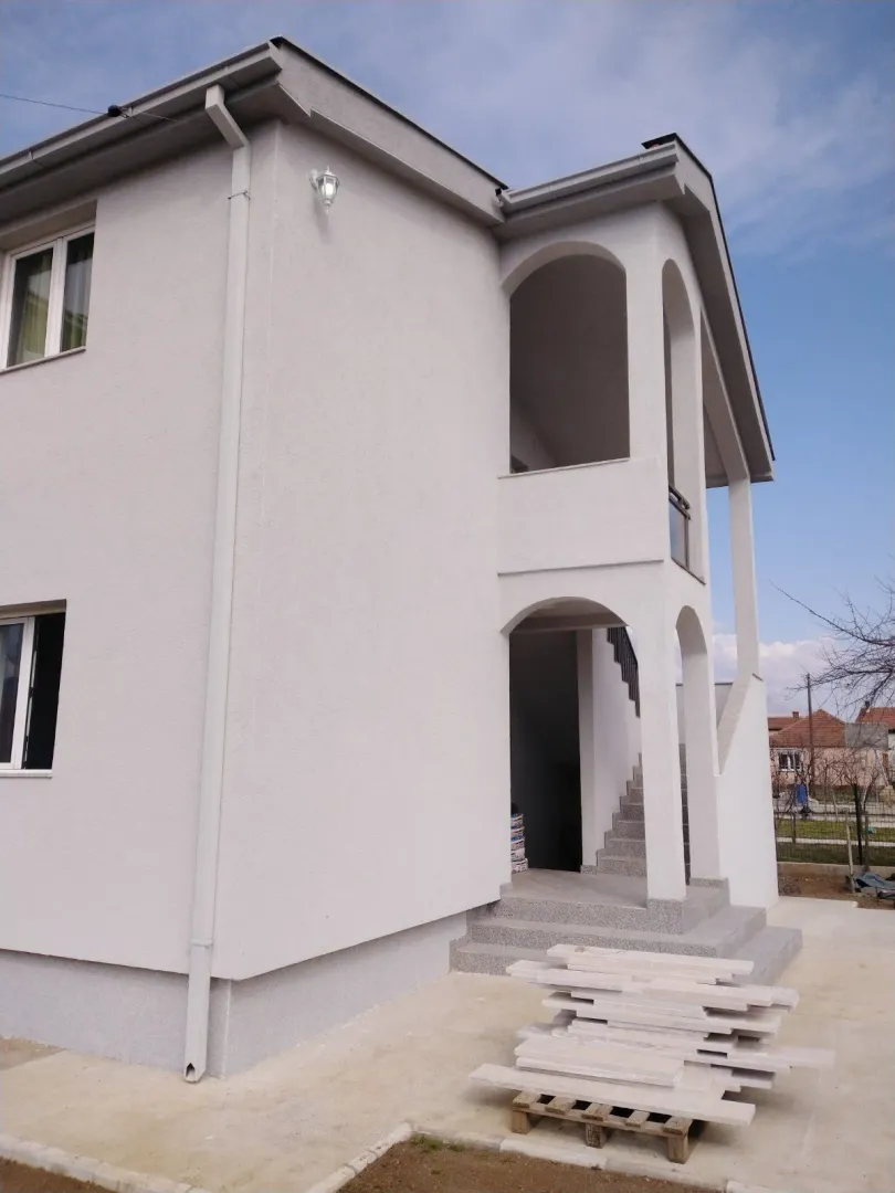 Bright facade of a two-story house with arched details and outdoor stairs.