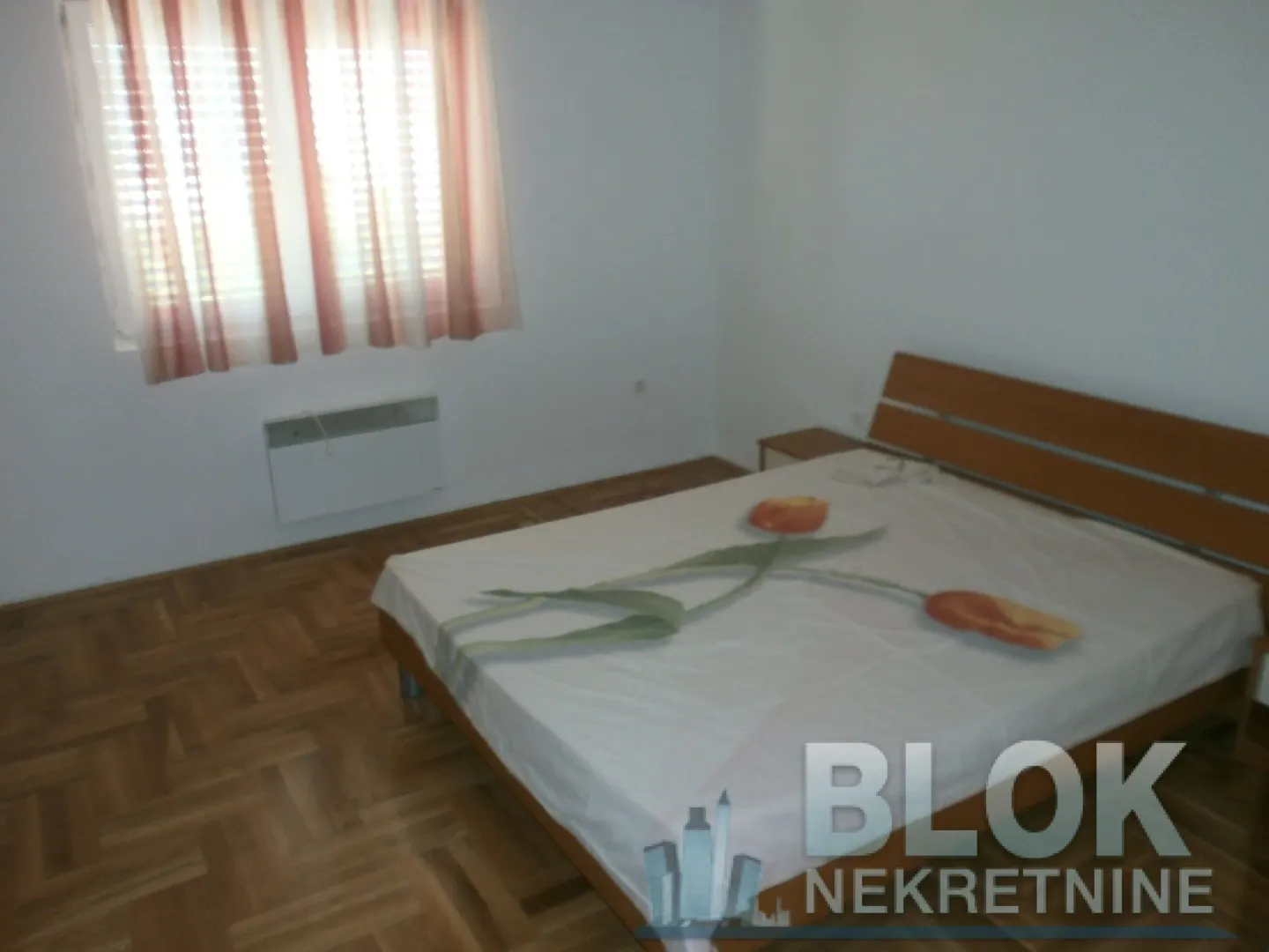 Bedroom with a double bed, wooden parquet flooring, and a window with curtains.