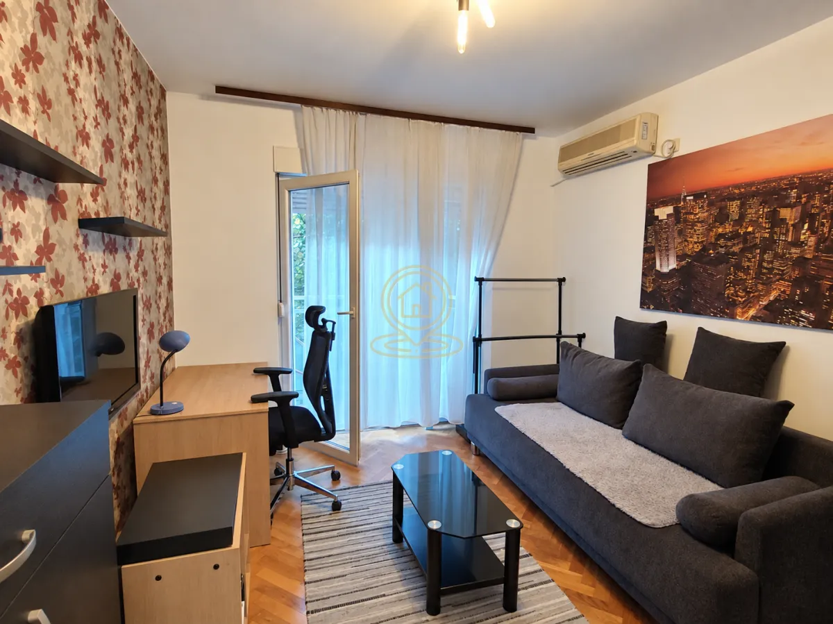 Dnevna soba sa ugaonom garniturom, radnim stolom i izlazom na terasu.