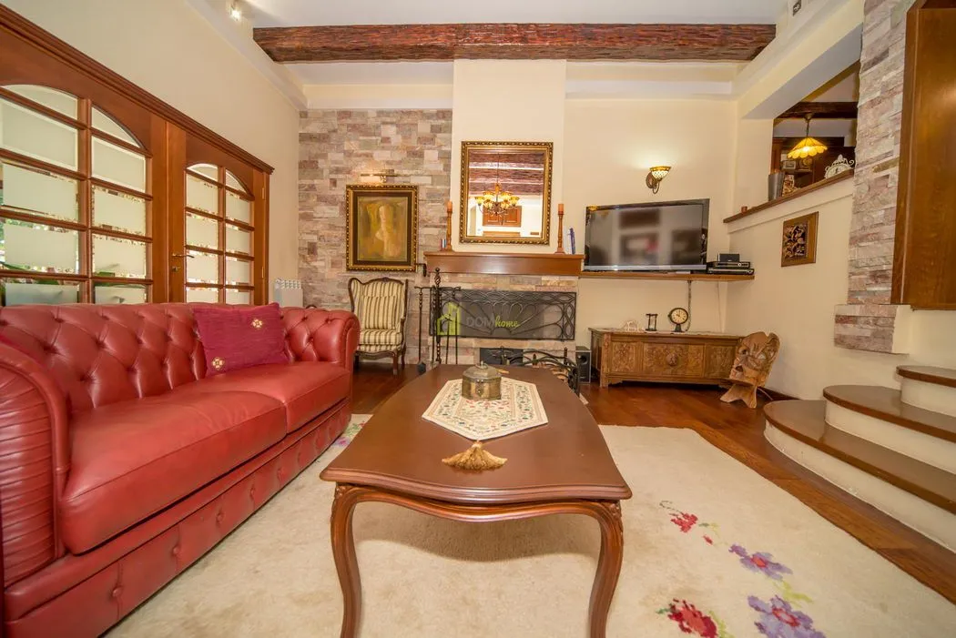 Living room with a red leather sofa, fireplace, and wooden ceiling beams.