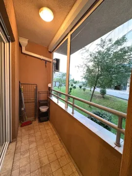 Natkriveni balkon sa pogledom na uređeno zeleno dvorište i okolne zgrade. - image 12