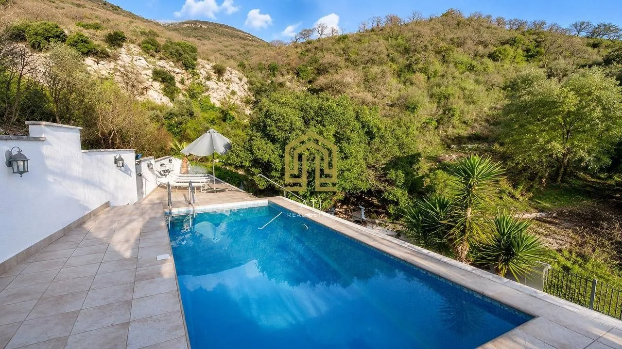 Outdoor swimming pool with a terrace and sun loungers surrounded by lush greenery.