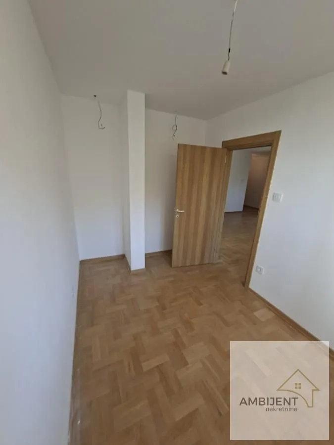 Prazna soba sa parketom i drvenim vratima.