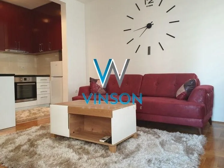 Dnevna soba sa garniturom, stočićem i velikim zidnim satom.