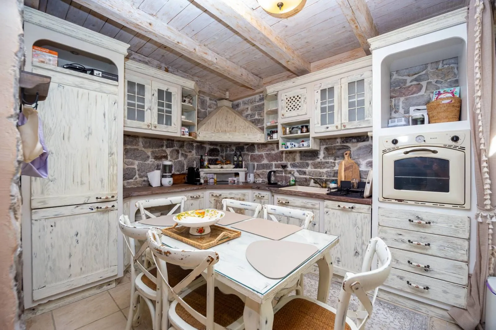 Rustic kitchen with a dining table, wooden beams, and stone walls.