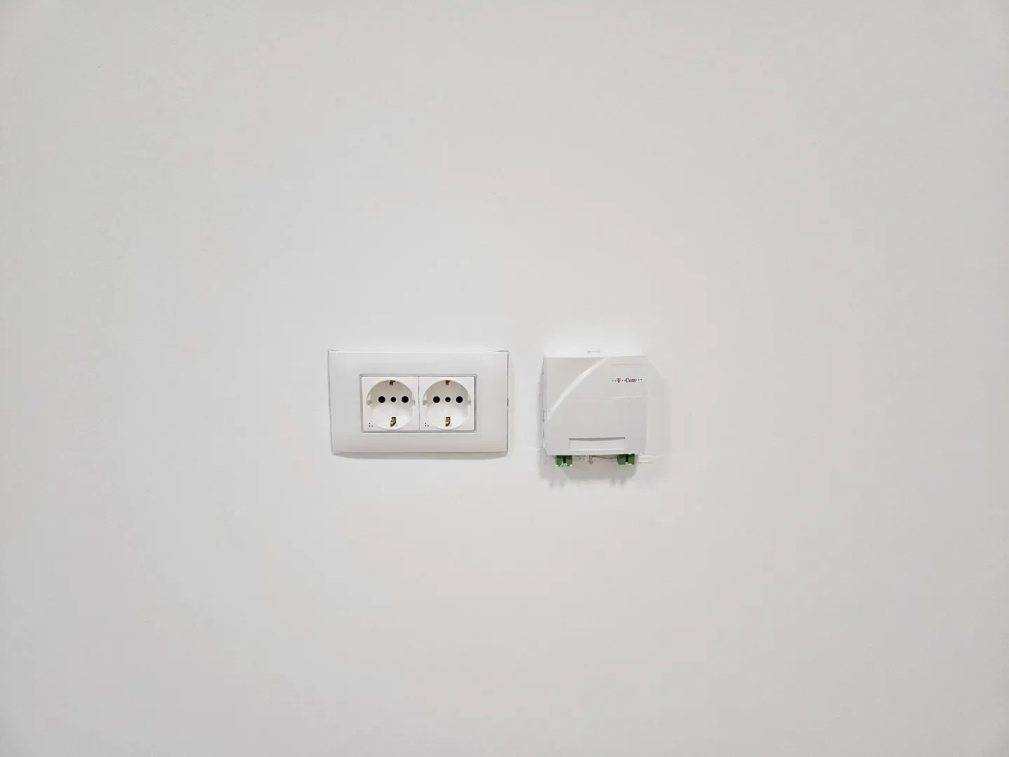 White wall with electrical outlet and telecommunication socket.