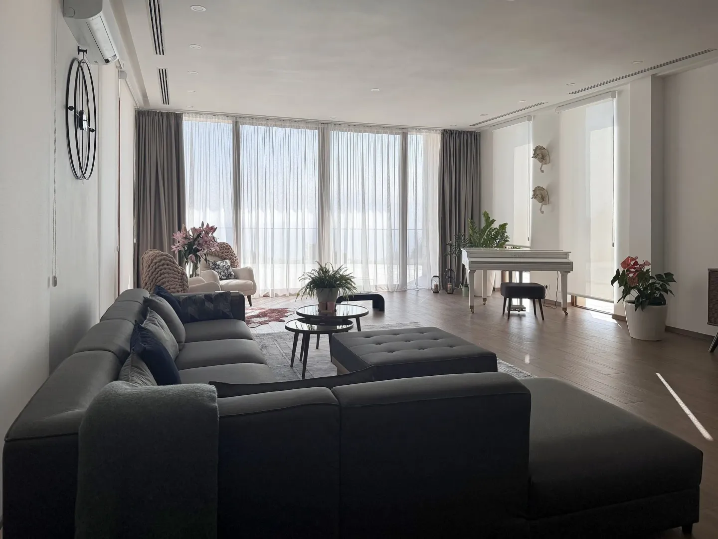 Spacious living room featuring a large sectional sofa, a piano, and large windows.