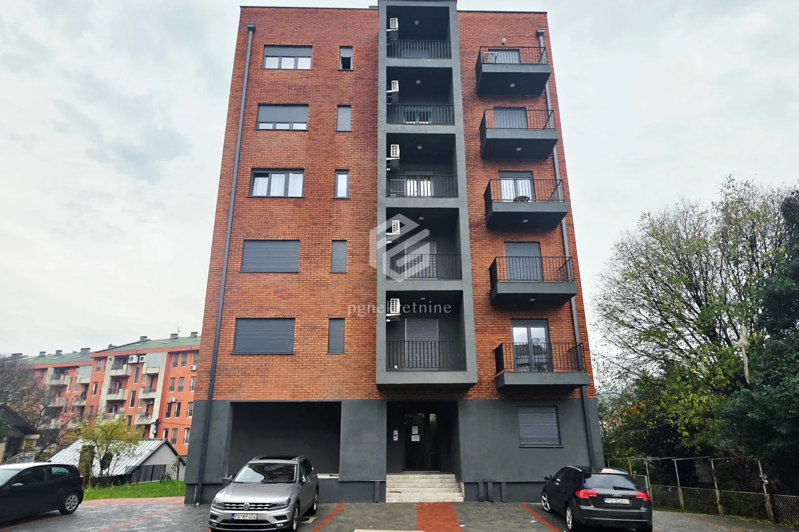 Brick residential building facade with balconies and parking area.