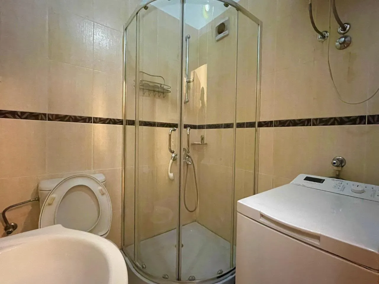 Smaller bathroom with a shower cabin, toilet, and washing machine.