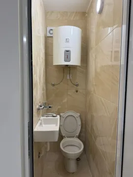 A small restroom featuring a wall-mounted water heater, a compact sink, and a toilet. - image 12