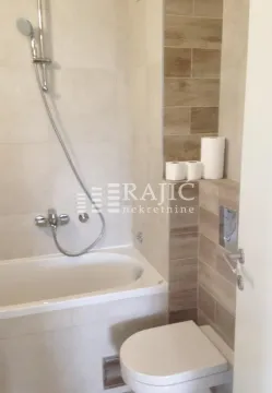 Small bathroom with a bathtub, toilet, and built-in shelves. - image 7