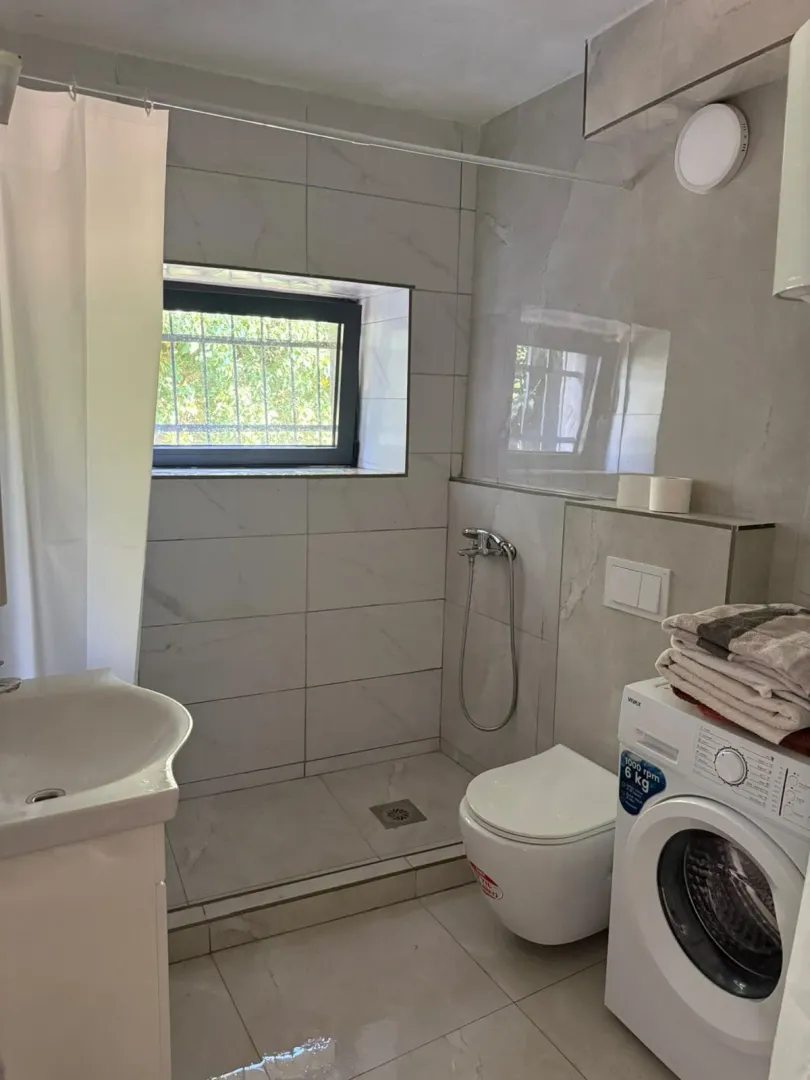 Manje kupatilo sa tuš kabinom, umivaonikom, WC šoljom i veš mašinom.