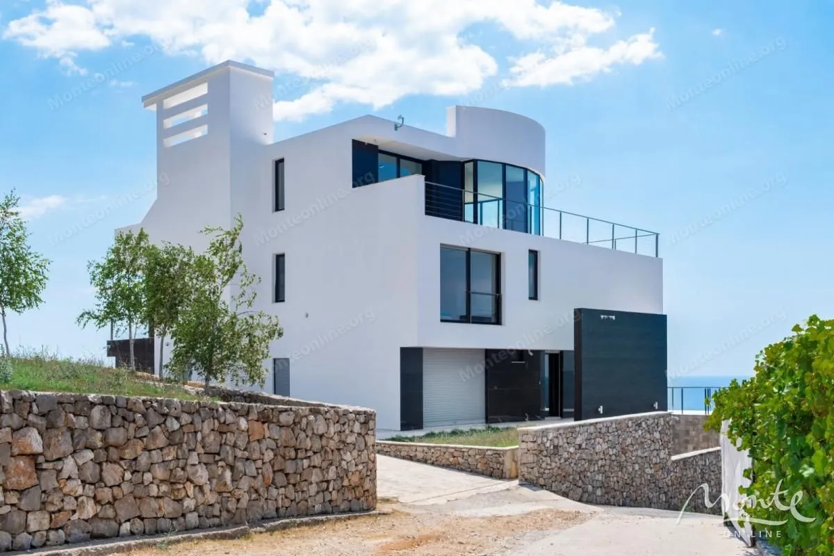 Exterior view of a modern white house with terraces and a stone wall.