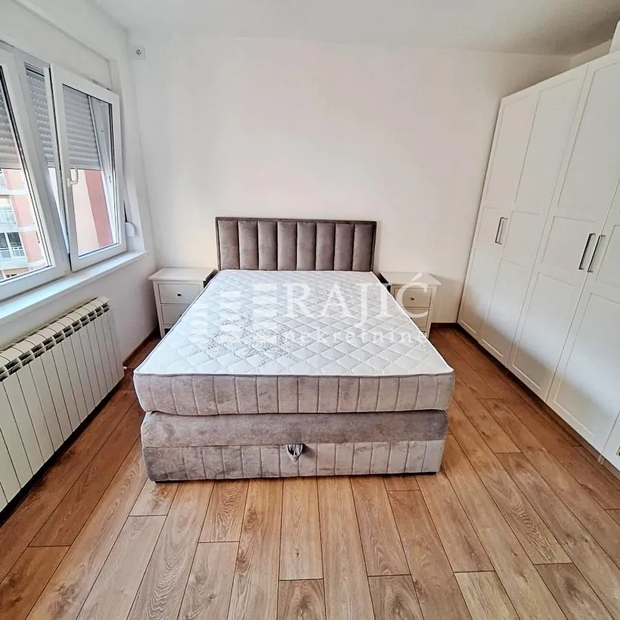 Furnished bedroom with a double bed, white wardrobe, and wooden flooring.
