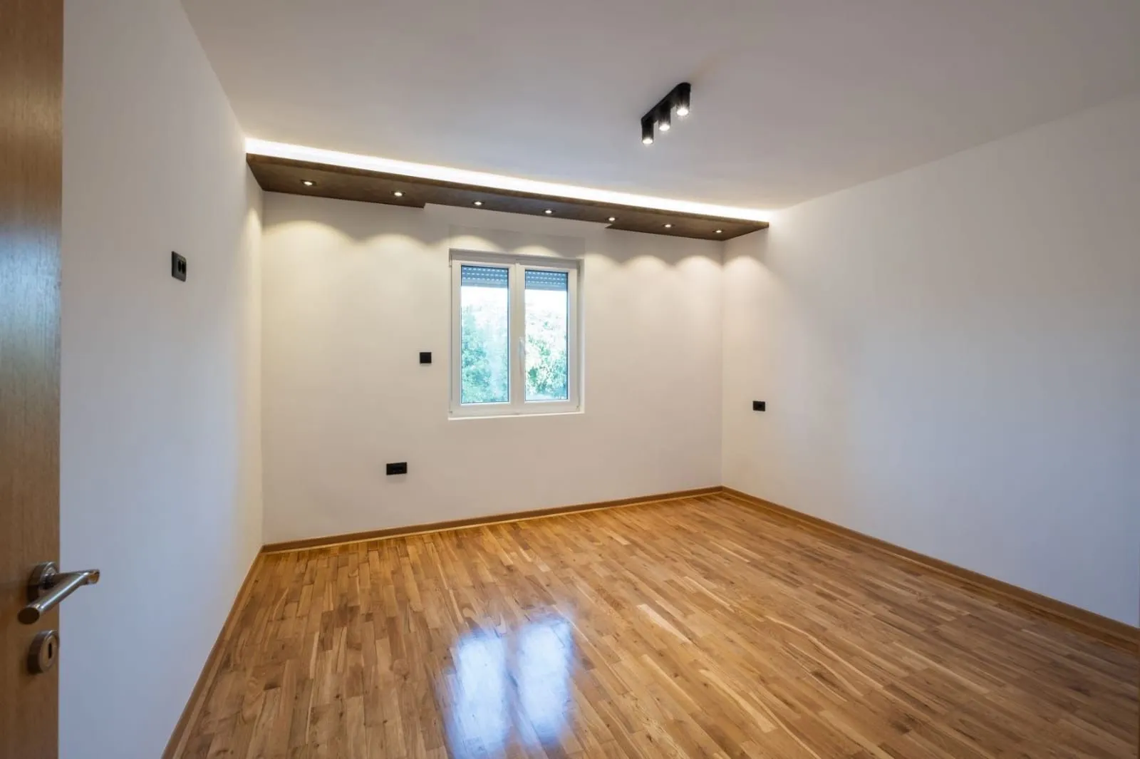 Empty room with hardwood flooring and recessed ceiling lighting.