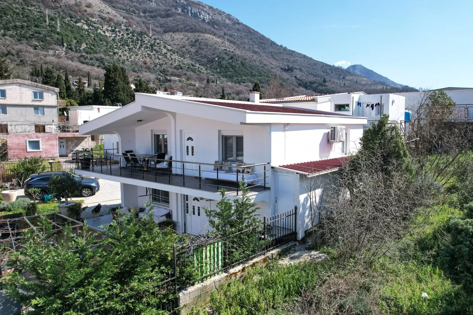 Pogled na bijelu dvospratnu kuću sa terasom i dvorištem.