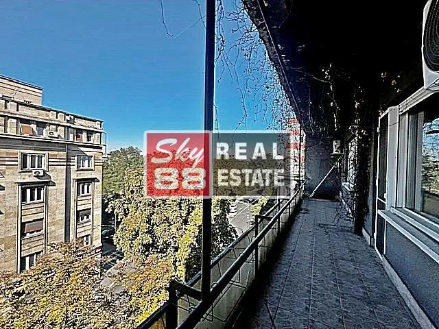 Long tiled balcony with a metal railing and a view of surrounding buildings and trees.