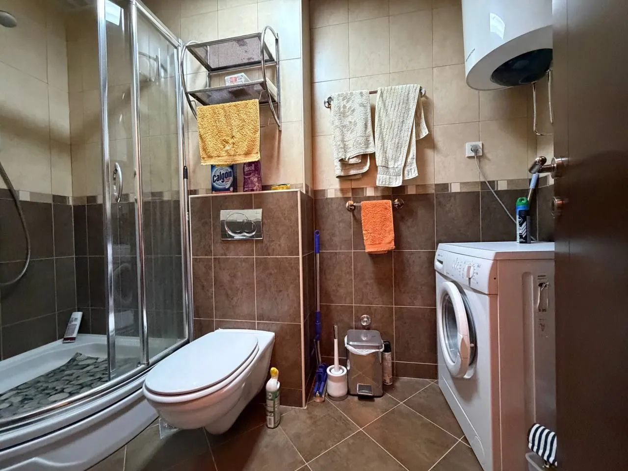 Manje kupatilo sa tuš kabinom, WC šoljom i veš mašinom.