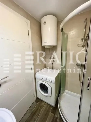 Smaller bathroom with a shower cabin, water heater, and washing machine.