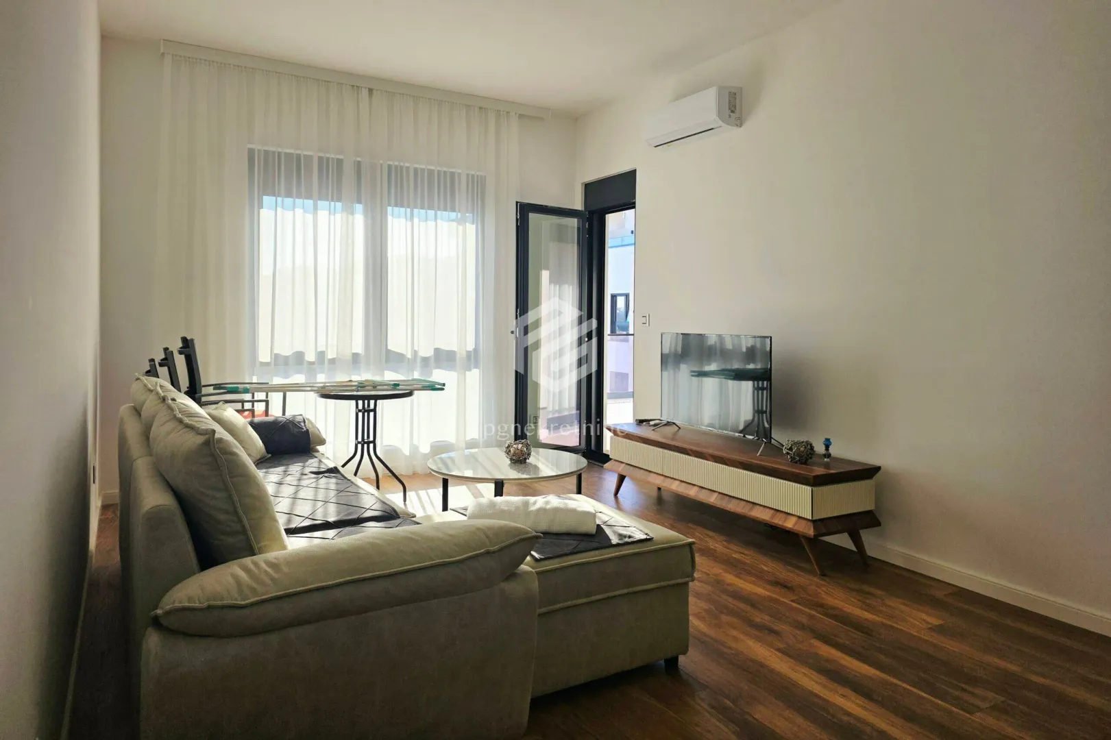 Living room with a corner sofa, TV unit, and access to the terrace.
