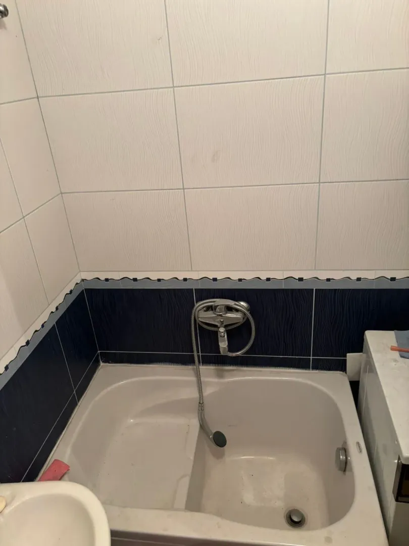 Manje kupatilo sa kadom obloženom pločicama i tuš baterijom.