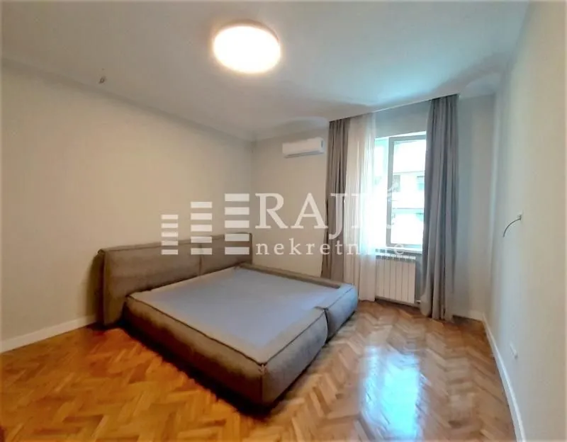 Bedroom with a double bed, parquet flooring, and a window with curtains.