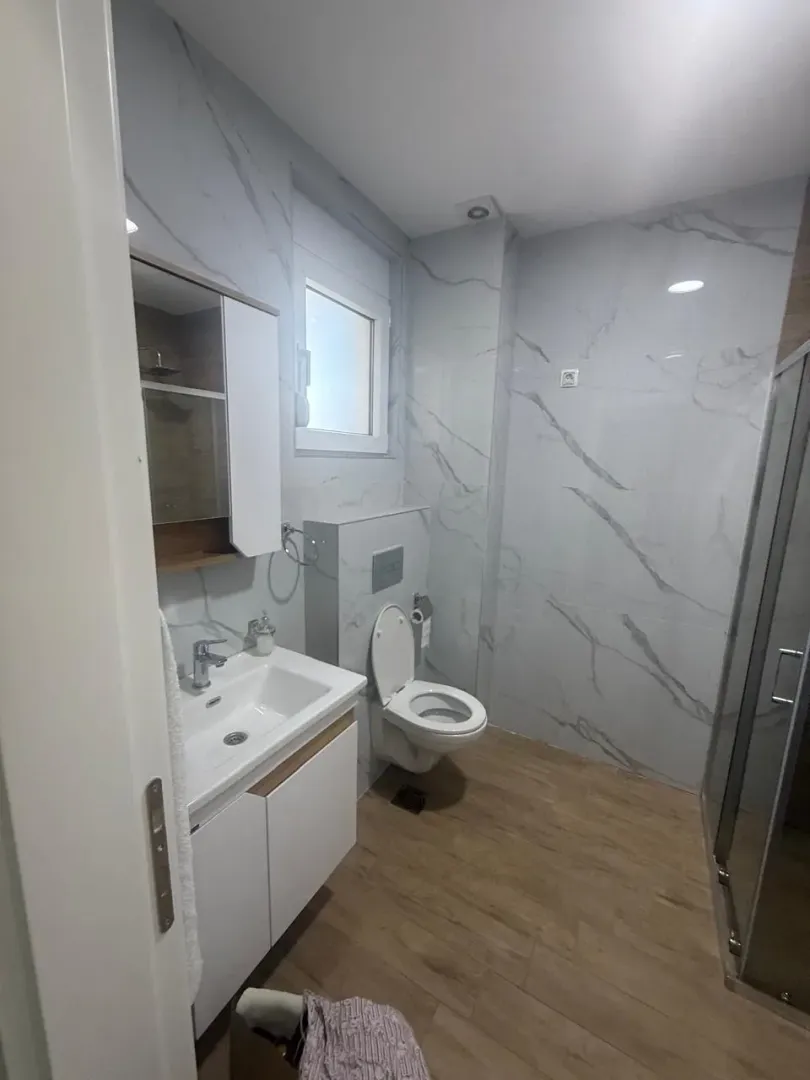 Moderno opremljeno kupatilo sa bijelim pločicama i tuš kabinom.