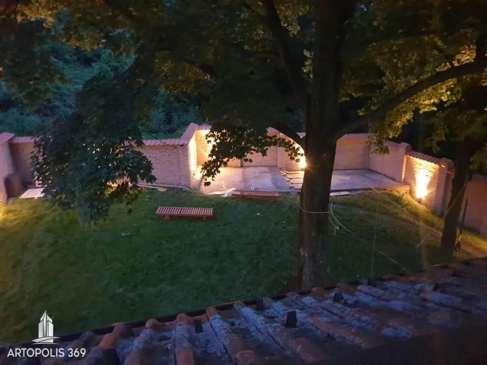 Noćni pogled na osvetljeno dvorište i travnjak sa drvećem.