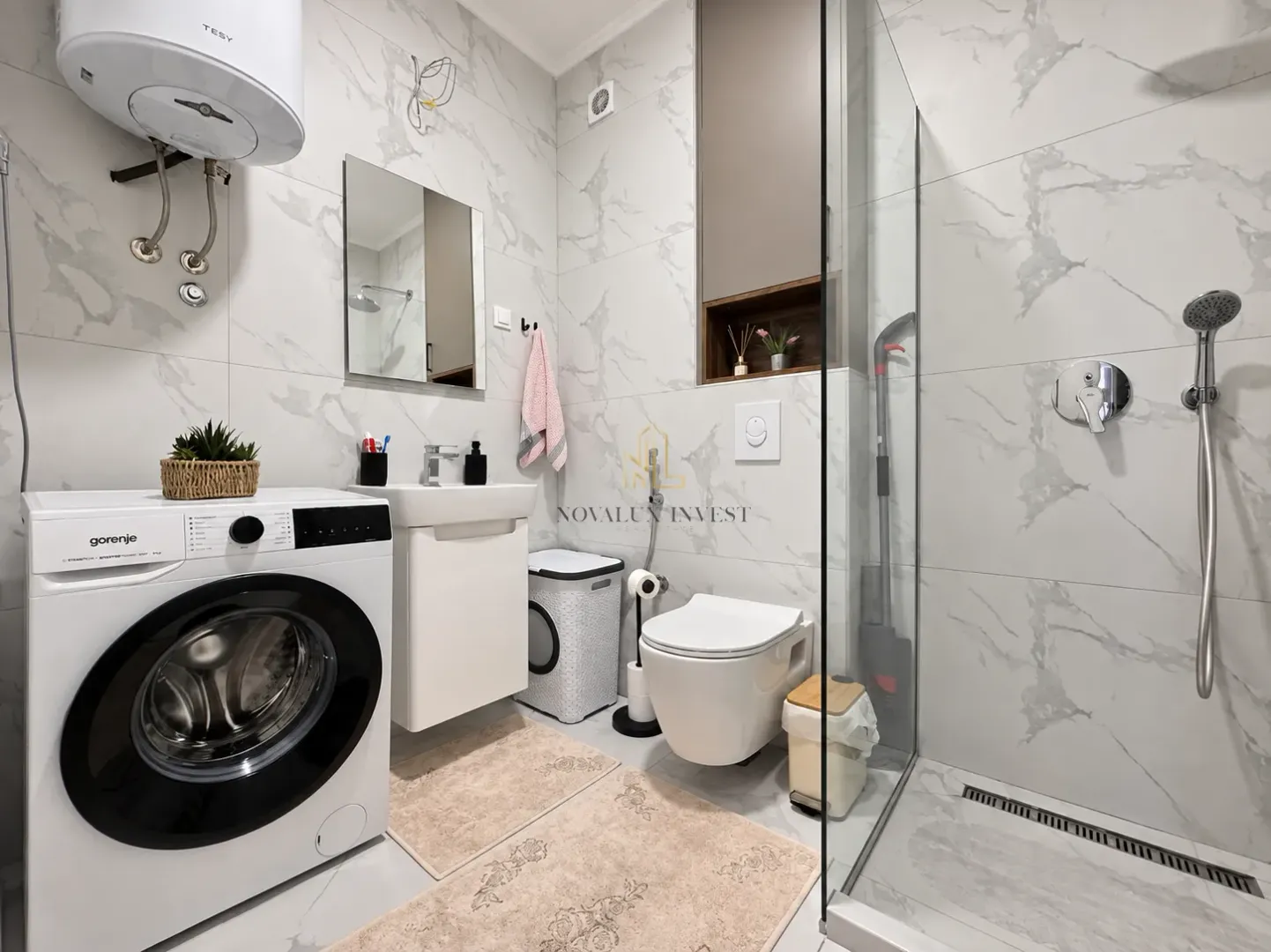 Modern bathroom equipped with a walk-in shower, washbasin, toilet, and washing machine.