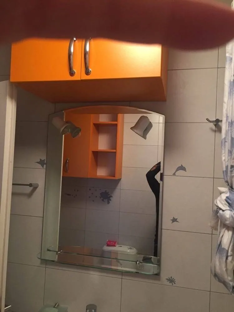 A bathroom featuring a mirror and an orange wall-mounted cabinet.